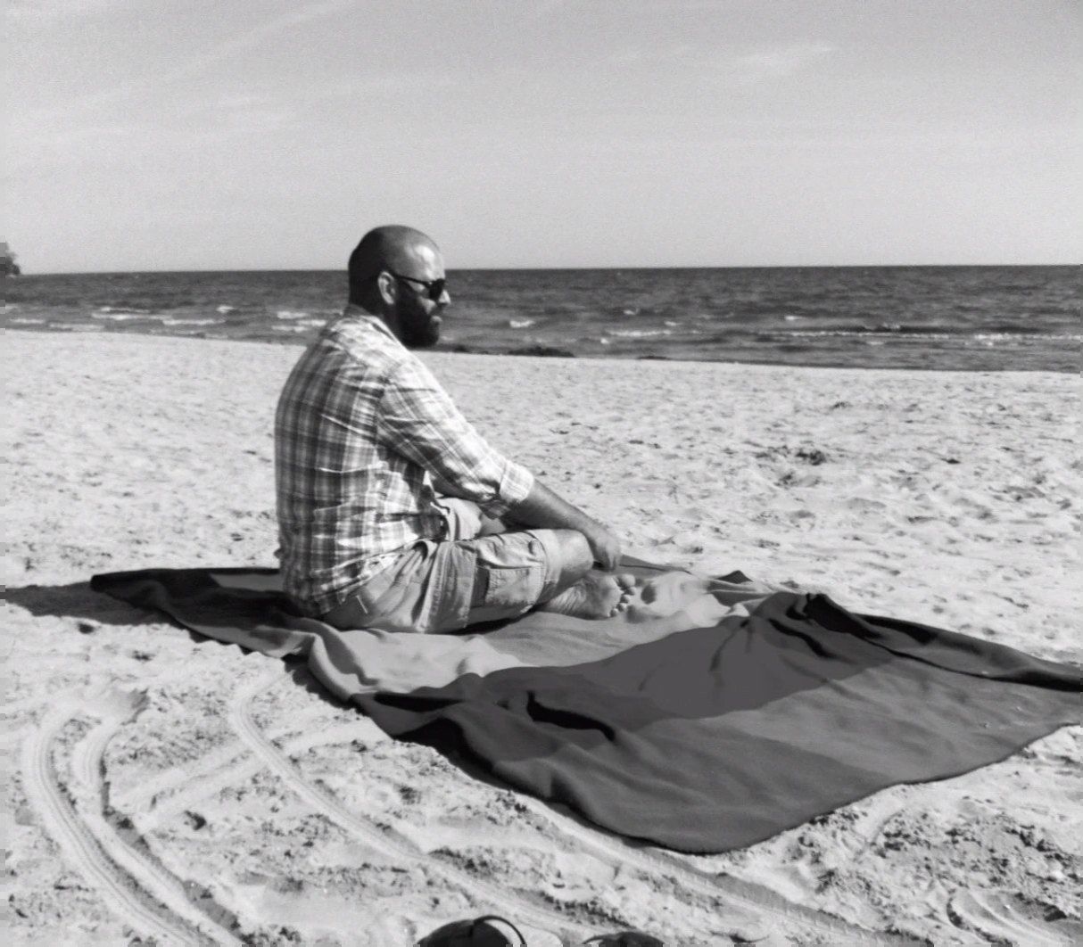 Adam Spencer sitting cross-legged on a blanket on a Lake Ontario beach, looking out at the water