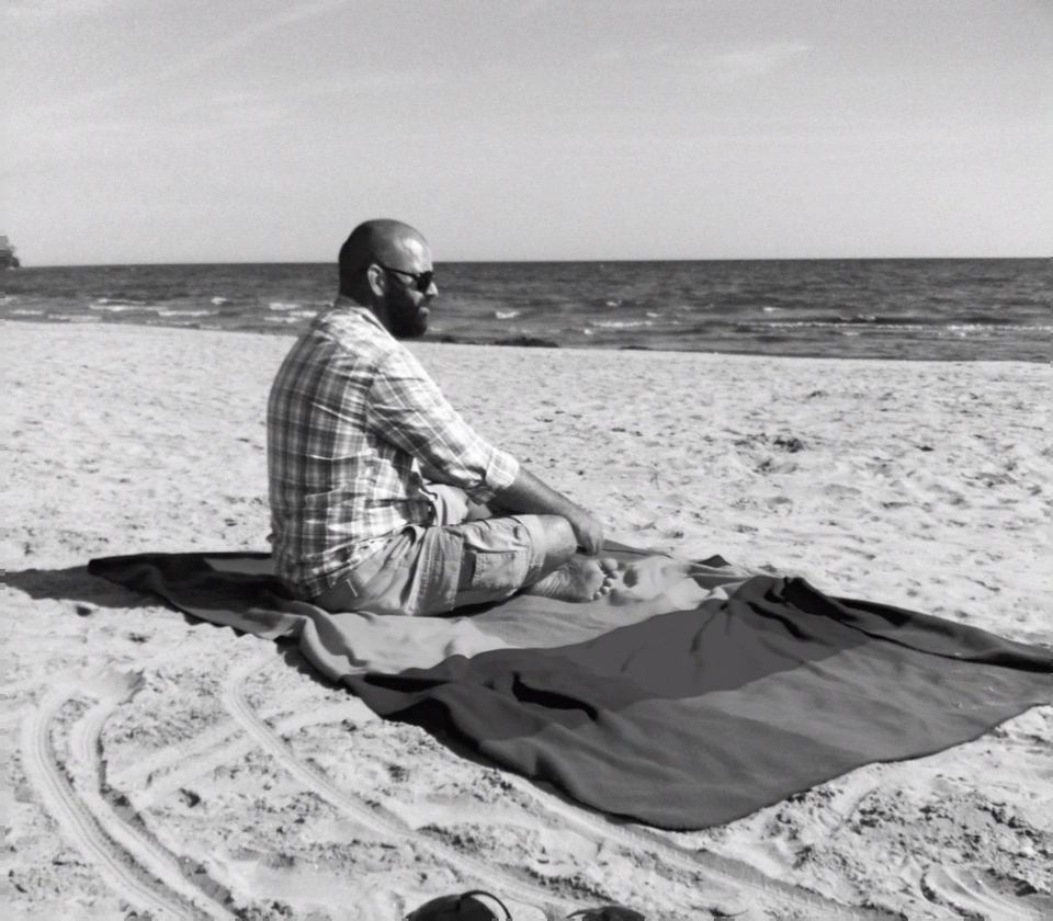 Adam Spencer sitting on a blanket on a Lake Ontario beach, looking out at the water